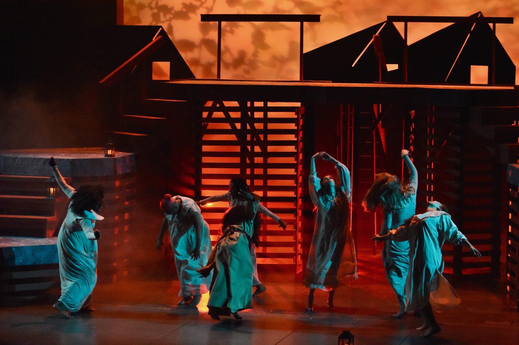 Students dancing on stage in white attire during a performance of the Crucible