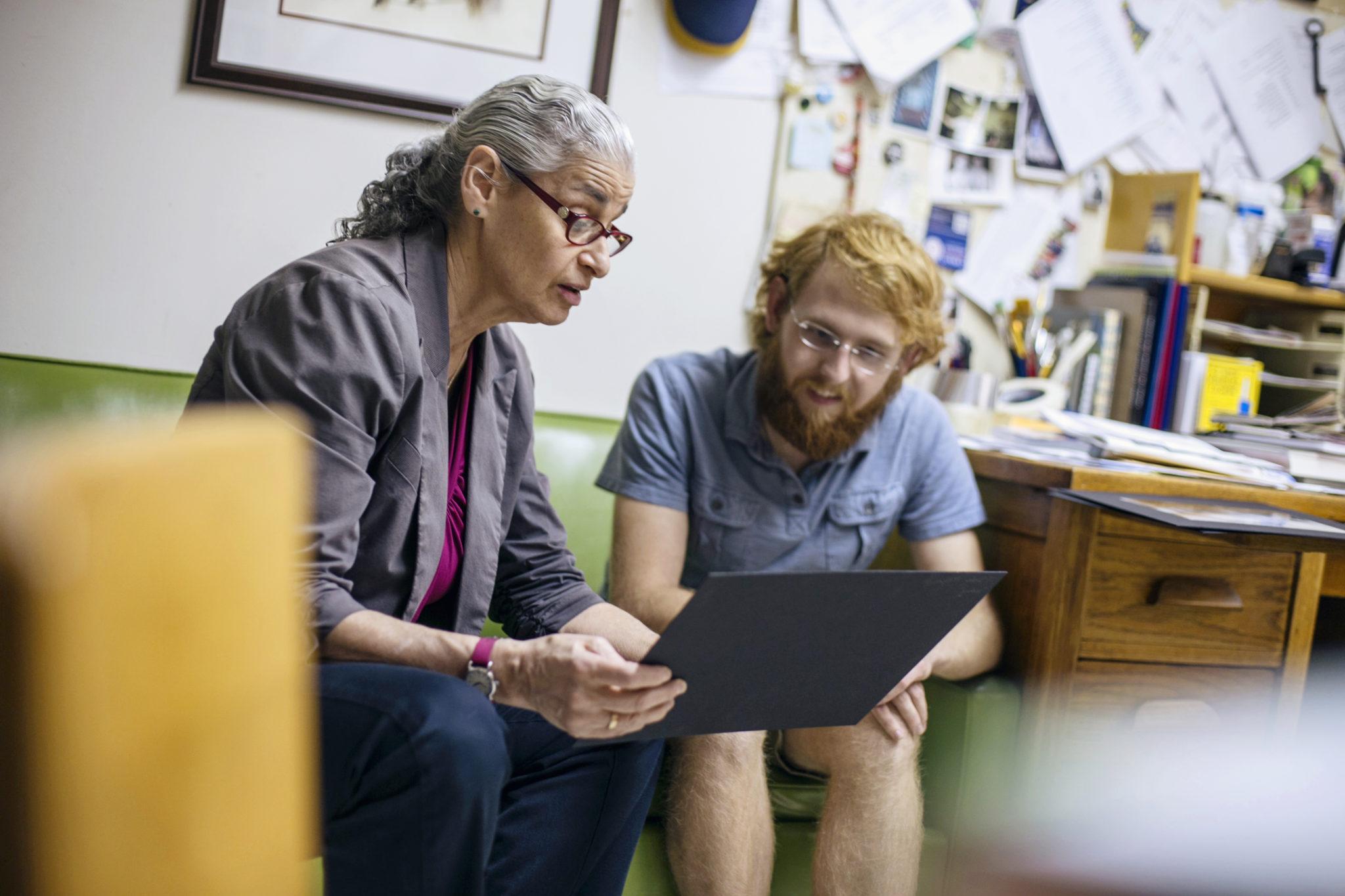 Student and professor seated on couch discussing artwork